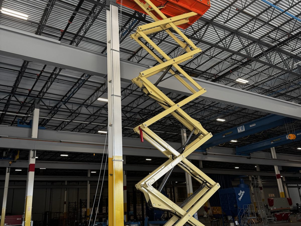 Scissor lift raised to the ceiling structure inside a high-bay warehouse building