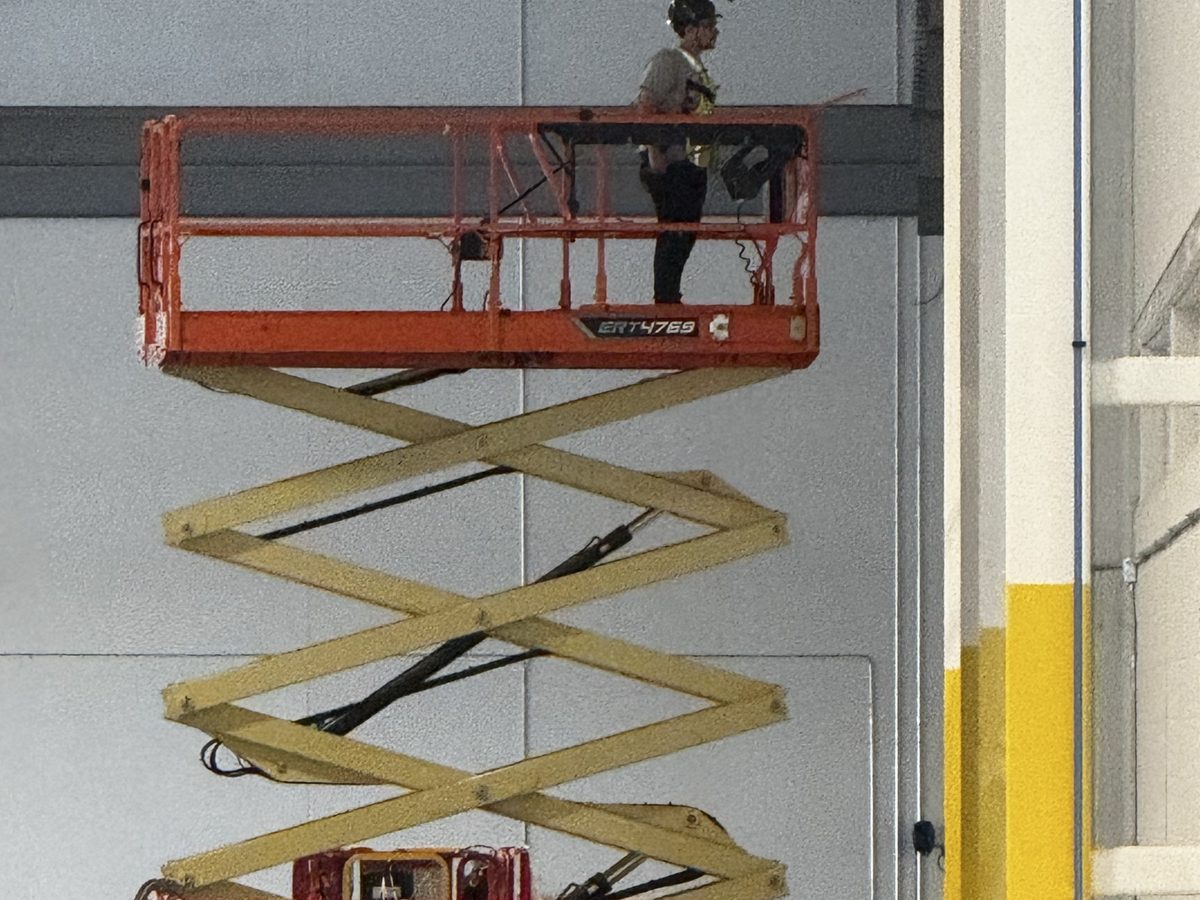 Technician on a scissor lift platform raised to ceiling height inside a commercial building